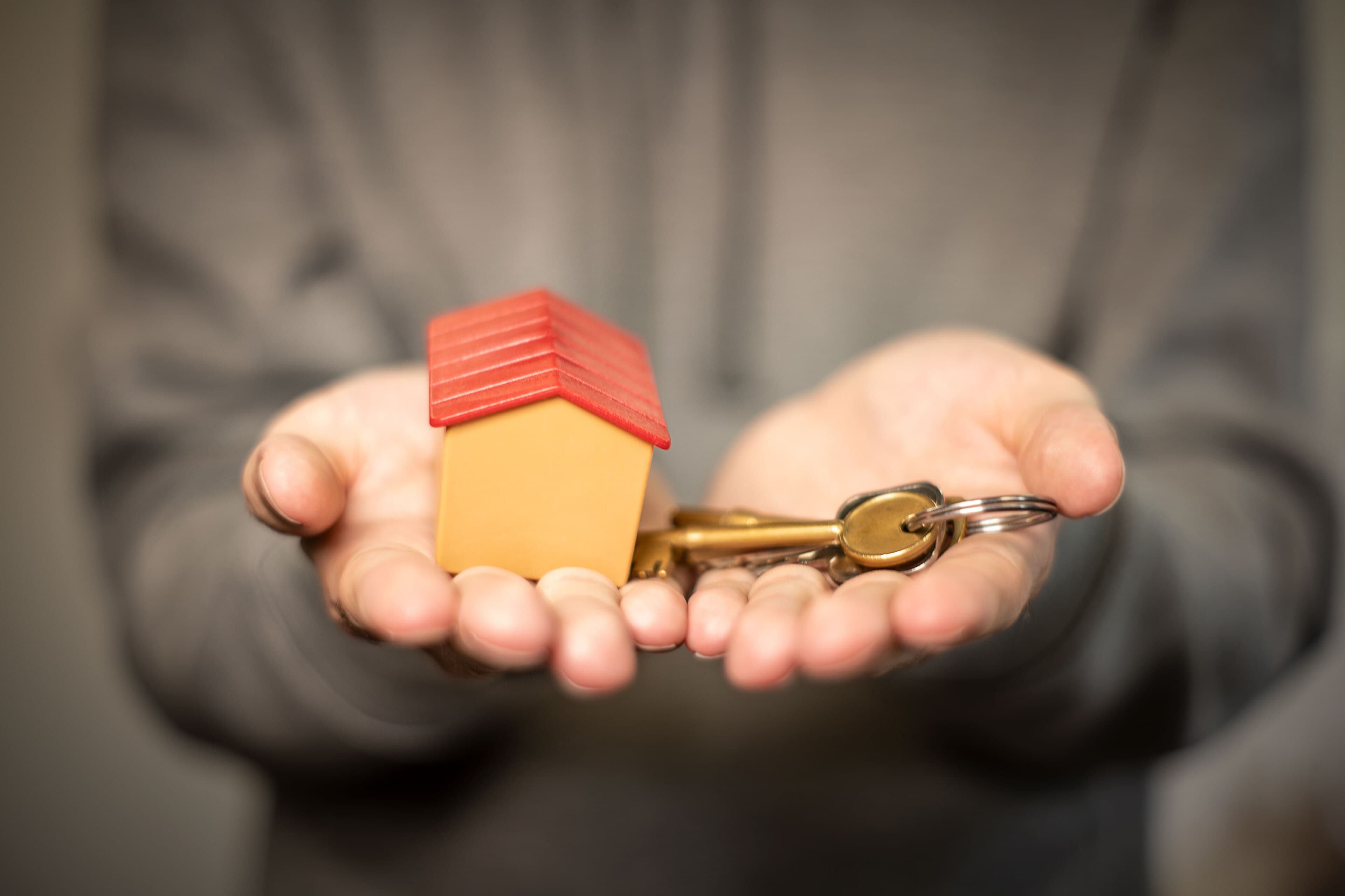 Two open hands holding a small model house and a set of keys